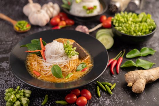 Chicken curry in a black cup with rice noodles.