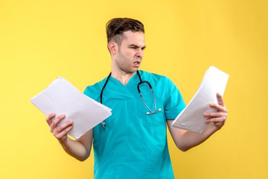 Front view of young male doctor with documents on a yellow wall