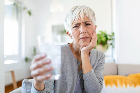 Senior woman with sensitive teeth and hand holding glass of cold water with ice healthcare concept mature woman drinking cold drink glass full of ice cubes and feels toothache pain