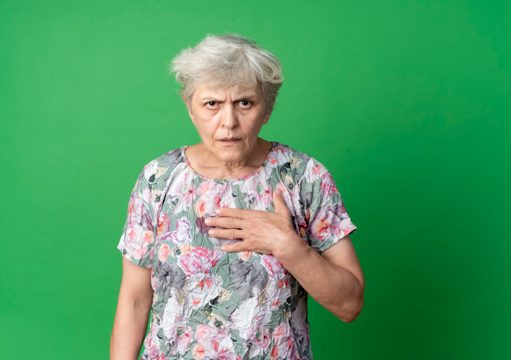Annoyed elderly woman puts hand on chin and looks isolated on green wall