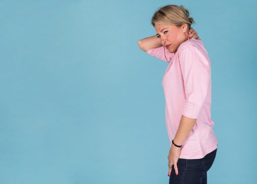 Side view of a woman suffering from neck pain against blue wallpaper