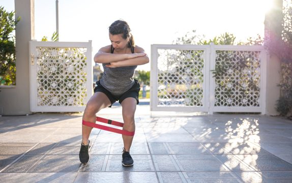 A young woman in a tank top and shorts goes in for sports with an expander in the open air.