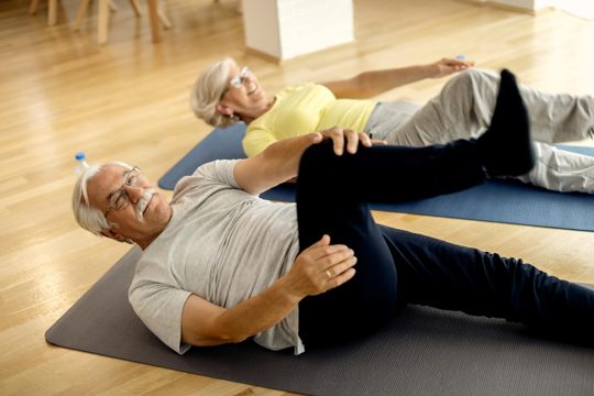 Smiling mature couple doing relaxation exercises on the floor at home