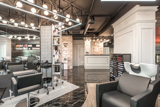 Backwash chair with sink placed near shelves with cosmetology products and reception desk in stylish beauty salon with decorated walls