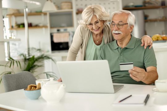 Happy mature couple using laptop and credit card while home shopping
