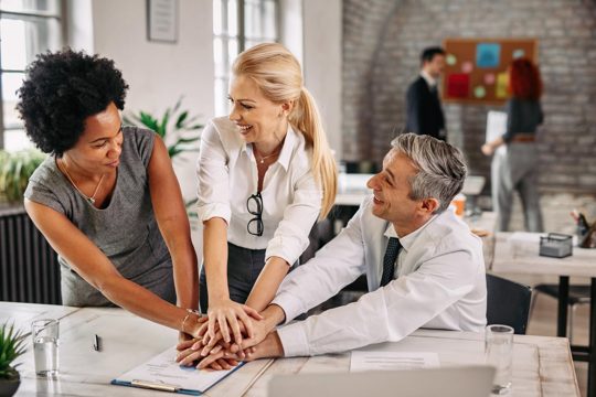 Group of happy business colleagues holding hands in unity after successful job there are people in the background