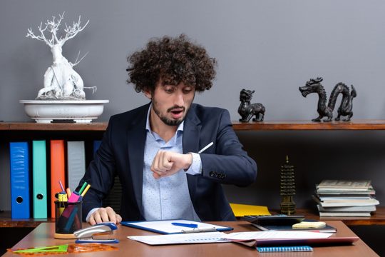 Front view of young businessman sitting at desk checking time