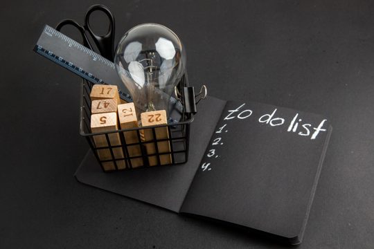 Bottom view office stuffs in pen case to do list written on black notepad on black table