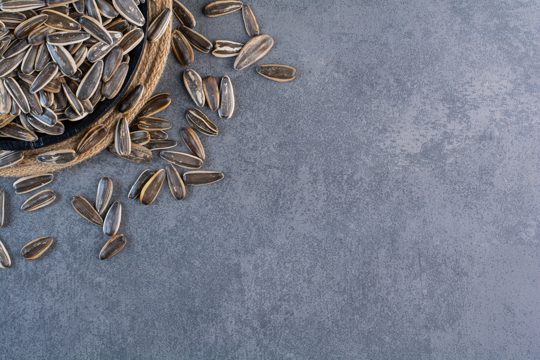 Black sunflower seeds in bowl on trivet , on the marble background.