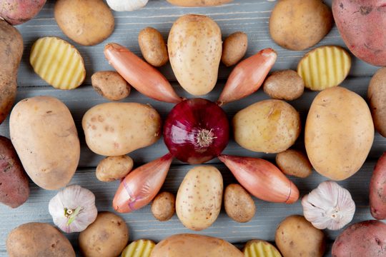 Top view of pattern of vegetables as sliced and whole potato shallot garlic and onion on wooden background