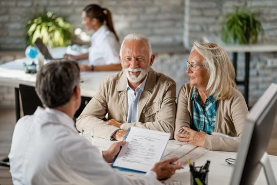 Happy senior couple communicating with a doctor about their health insurance while going through paperwork