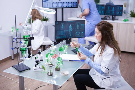 Female scientist holding a green solution while hear team works in the background. young biologist in the background.