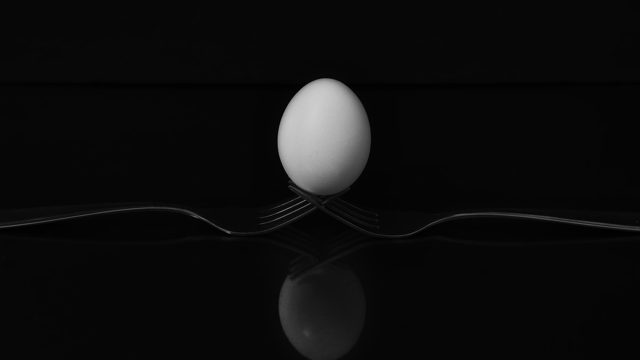 Grayscale shot of an egg on two forks